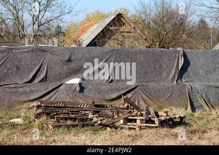 Stapel gebrochener Holzpaletten vor einem vorübergehenden Hochwasser Schutzwand aus Kastenbarrieren und Sandsäcken mit abgedeckt Dicker Geotextil-Stoff Stockfoto