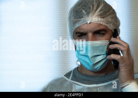 Ein Arzt spricht am Telefon mit einem besorgten Gesichtsausdruck, der in persönlicher Schutzausrüstung (PSA) gekleidet ist. COVID-19 Konzept Stockfoto
