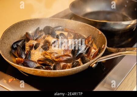 Miesmuscheln in Sahne- und Weißweinsauce werden auf dem Herd in einer Wok-Pfanne gekocht. Selektiver Fokus. Stockfoto