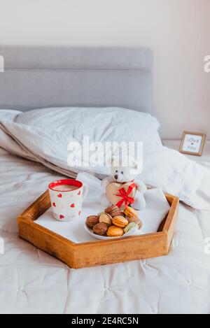 Valentinstag Frühstück im Bett für Liebhaber. Teddybär mit einer herzförmigen Geschenkbox mit rotem Band, einer Tasse Kaffee und Makronen-Kekse auf dem Stockfoto