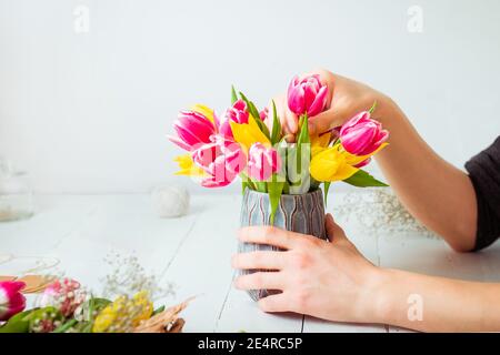 Kein Gesicht junger Mann, der Frühlingsstrauß mit Tulpen macht. Online-Selbstbildung von Floristik. Blumenarranging lernen. Lieferung von Blumen. Männlicher Blumenhändler Stockfoto