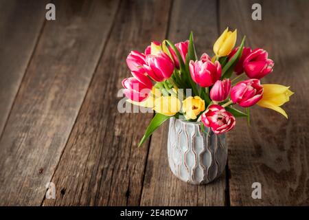 Frisches Frühlingsgelb und rosa Tulpen Bouquet in blauer Vase auf rustikalem Holztisch Hintergrund stehen. Festliche Blumen für den Mutter- oder Frauentag Stockfoto