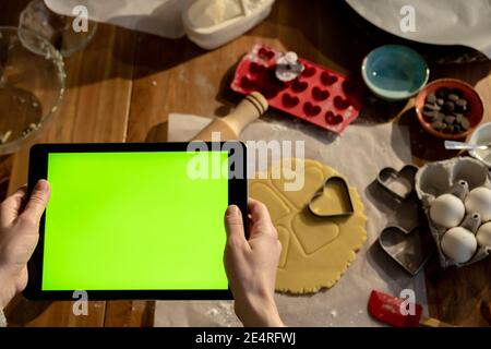 Frau hält Tablet mit grünem Bildschirm in der Hand Uhren Bildung. Cookie Zutaten im Hintergrund. Stockfoto