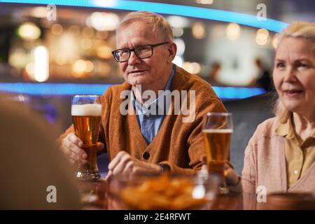Porträt eines lächelnden älteren Mannes, der in der Bar Bier trinkt, während er den Abend mit Freunden genießt, Platz zum Kopieren Stockfoto