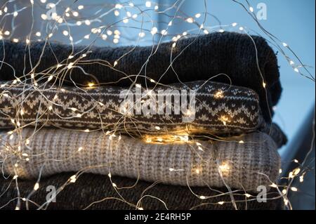 Nahaufnahme von LED-Leuchten Girlande auf Stapel von gemütlichen Strickpullover. Hygge warm consept. Stockfoto