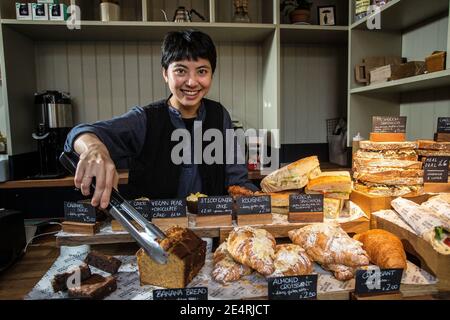 Attraktive Barista lächelt am Bäckereitisch und schlägt Kuchen in einem modernen Café oder Restaurant vor. Stockfoto