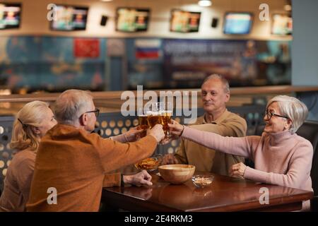 Eine Gruppe lächelnder älterer Menschen, die in der Bar Bier trinken und in die Gläser klirren, während sie mit Freunden ausklingen, Platz zum Kopieren Stockfoto