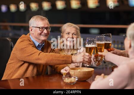 Porträt eines lächelnden älteren Ehepaares, das in der Bar Bier trinkt, und klirrende Gläser, während man mit Freunden ausgeht und Platz kopiert Stockfoto