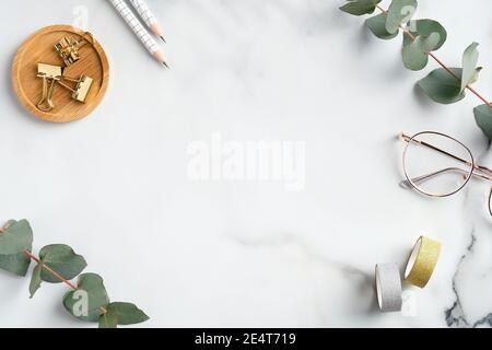 Flacher Schreibtisch für das Home Office. Femininer Arbeitsplatz mit Brille, Bürobedarf, Grün auf Marmorhintergrund. Eleganter Freiberufler-Arbeitsplatz Stockfoto