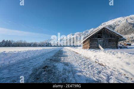 Schneebedeckter Wanderweg durch sonnige alpine Winterlandschaft mit Holzscheune in Wildermieming, Tirol, Österreich Stockfoto