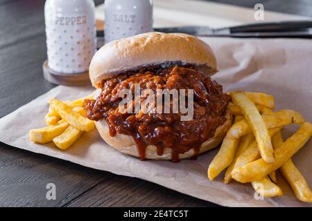 Heißes, frisch zubereitetes Schweinebrill-Sandwich mit französischen Bratkartoffeln auf braunem Papier Stockfoto