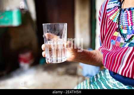 Eine ältere Frau trinkt ein Glas sauberes Wasser in San Juan la Laguna, Guatemala, Mittelamerika. Stockfoto