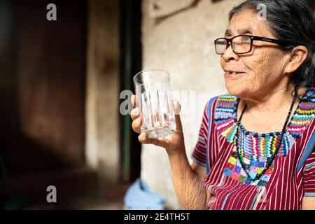 Eine ältere Frau trinkt ein Glas sauberes Wasser in San Juan la Laguna, Guatemala, Mittelamerika. Stockfoto