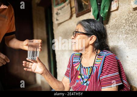 Eine ältere Frau trinkt ein Glas sauberes Wasser in San Juan la Laguna, Guatemala, Mittelamerika. Stockfoto