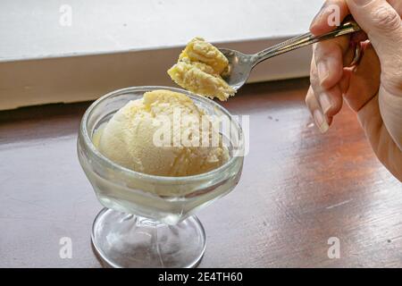 Die Nahaufnahme von leckeren hausgemachten kühlen Vanille-Eis Schaufel in Glas Tasse auf Vintage Holz Tisch Hintergrund Stockfoto
