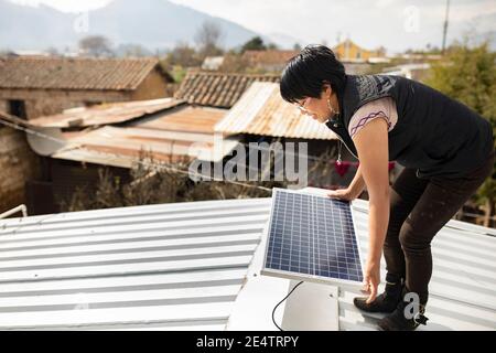 Ein Techniker von einem lokalen gemeinnützigen Energieversorger installiert ein neues solarbetriebenes Beleuchtungssystem auf einem Haus in Cantel, Guatemala. Stockfoto