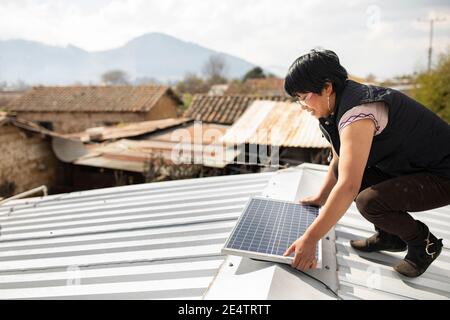 Ein Techniker von einem lokalen gemeinnützigen Energieversorger installiert ein neues solarbetriebenes Beleuchtungssystem auf einem Haus in Cantel, Guatemala. Stockfoto