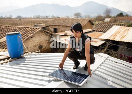 Ein Techniker von einem lokalen gemeinnützigen Energieversorger installiert ein neues solarbetriebenes Beleuchtungssystem auf einem Haus in Cantel, Guatemala. Stockfoto