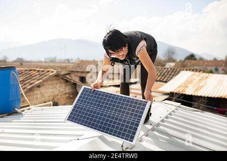 Ein Techniker von einem lokalen gemeinnützigen Energieversorger installiert ein neues solarbetriebenes Beleuchtungssystem auf einem Haus in Cantel, Guatemala. Stockfoto