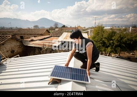 Ein Techniker von einem lokalen gemeinnützigen Energieversorger installiert ein neues solarbetriebenes Beleuchtungssystem auf einem Haus in Cantel, Guatemala. Stockfoto