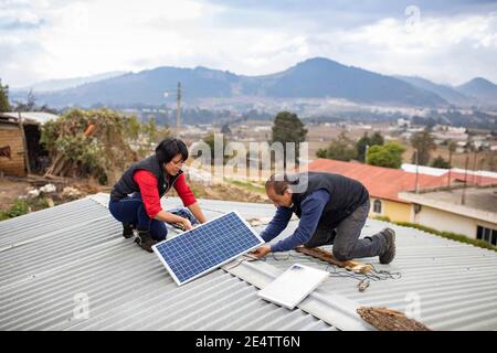 Techniker von lokalen gemeinnützigen Energieunternehmen installieren eine neue solarbetriebene Beleuchtung auf einem Haus in Cantel, Guatemala, Cen Stockfoto