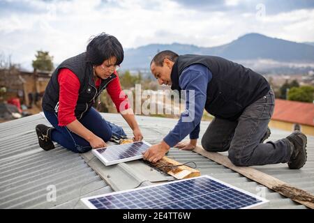 Techniker von lokalen gemeinnützigen Energieunternehmen installieren eine neue solarbetriebene Beleuchtung auf einem Haus in Cantel, Guatemala, Cen Stockfoto