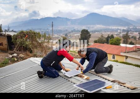 Techniker von lokalen gemeinnützigen Energieunternehmen installieren eine neue solarbetriebene Beleuchtung auf einem Haus in Cantel, Guatemala, Cen Stockfoto