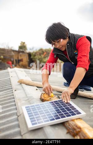 Ein Techniker von lokalen gemeinnützigen Energieunternehmen installiert ein neues solarbetriebenes Beleuchtungssystem auf einem Haus in Cantel, Guatemala, CE Stockfoto