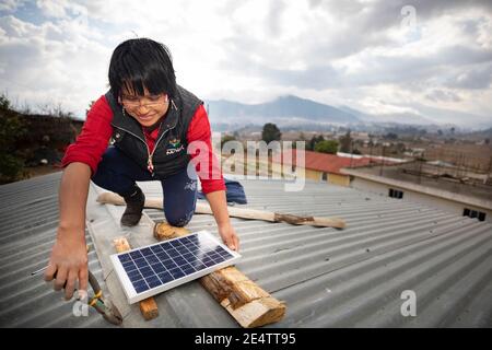 Ein Techniker von lokalen gemeinnützigen Energieunternehmen installiert ein neues solarbetriebenes Beleuchtungssystem auf einem Haus in Cantel, Guatemala, CE Stockfoto