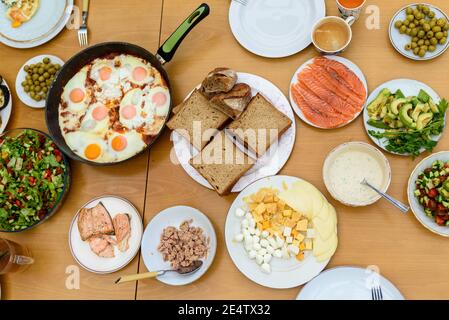 Gesundes Frühstück mit der Familie. Draufsicht. Servieren von Eiern, Brot, Avocado, geräuchertem Lachs, Käse und Salat aus frischem Gemüse auf einem Holztisch, Stockfoto