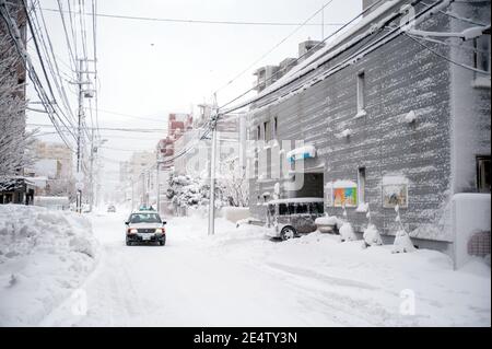 Ein Taxi fährt durch eine verschneite Straße in einer japanischen Stadt. Stockfoto