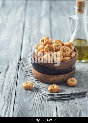 Traditionelle italienische Snack Taralli oder Tarallini in Holzschale über alten grauen Holztisch. Rustikale Schuss Taralli Vorspeise mit Kopierraum. Vertikal. Stockfoto