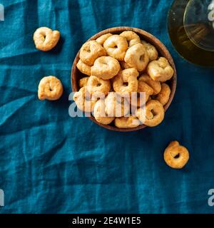 Traditionelle italienische Snack Taralli oder Tarallini in Holzschale über dunkelblauem Leinen Serviettenhintergrund. Rustikale Schuss Taralli Vorspeise mit Kopierraum. Ansicht von oben oder flach liegend. Quadratisches Erntegut Stockfoto