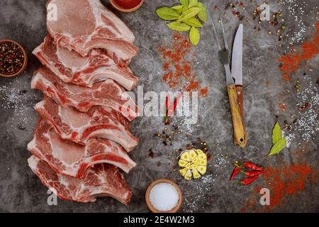 Scheiben rohe Schweinekotelett Rippe mit Gewürzen und Messer auf grauem Hintergrund. Draufsicht. Stockfoto