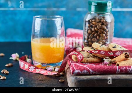 Chocolate Chips Plätzchen, Kaffeebohnen in einem Glas und ein Glas Orangensaft auf einem dunklen Tisch Stockfoto