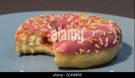Rosa süße Donut oder Donut mit farbigen Streuseln auf einem blauen Hintergrund. Gebissen von amerikanischem Bagel. Stockfoto