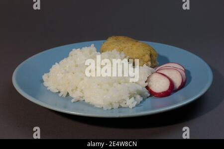 Gekochter weißer Reis mit Fischschnitzel in Speck auf einem grauen Hintergrund blauen Teller eingewickelt. Fischball mit Reisgarnieren und Rettich. Stockfoto