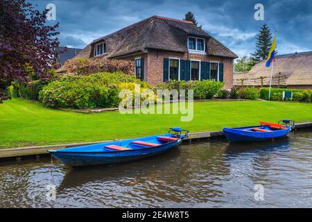 Festgefahrenen Motorboote auf dem Wasserkanal und niedlichen Uferhaus mit Ziergarten, Giethoorn, Niederlande, Europa Stockfoto