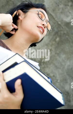 Smart aussehende asiatische Geschäftsfrau hält Stapel von Literatur und Ein Bleistift auf einem dunklen Wandhintergrund, der begeistert aufschaut Für die bevorstehende Veranstaltung Stockfoto