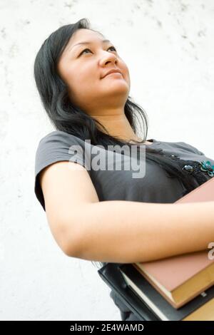 Porträt einer glücklichen asiatischen Studentin, die lächelt, während sie Bücher hält und aus der Ferne blickt (die Zukunft) mit weißem Hintergrund Stockfoto