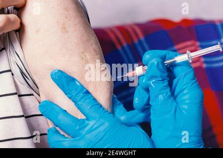 Sehr alter Mann bekommt Coronavirus-Impfstoff. Nahaufnahme. Injektion an ältere Menschen zu Hause. Spritze mit Medizin Ärzte Hände in blauen Handschuhen. Stockfoto