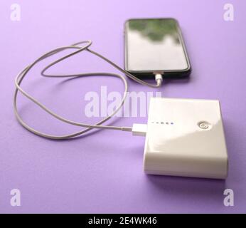 Handy wird von der Powerbank aufgeladen. Isoliert. Auf violettem Hintergrund. Stockfoto