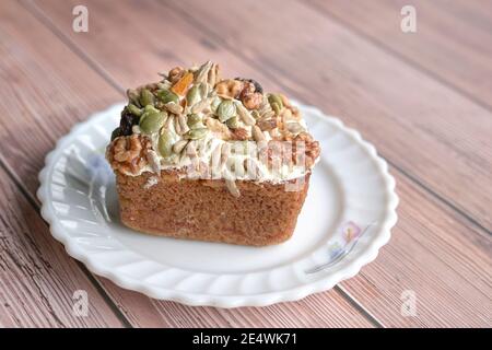 Karottenkuchen mit gemischten Nüssen, Samen und getrockneten Früchten als Belag. Isoliert. Auf Holztisch. Stockfoto