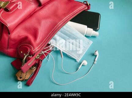 Frau rote Handtasche mit Gesichtsmaske, Handdesinfektionsmittel, Ohrhörer und Smartphone. Draufsicht. Stockfoto