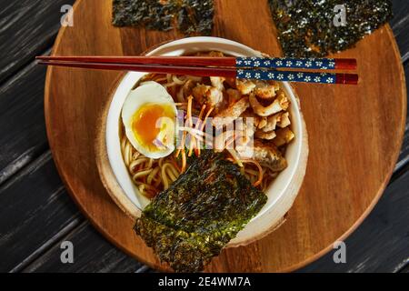 Japanische Ramen-Suppe mit Huhn, Ei, Knoblauch und Nudeln auf dunklem Holzgrund. Asiatische Miso Ramen Nudeln Stockfoto