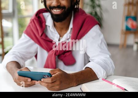 Fröhlich afroamerikanischen Kerl lächeln und spielen Videospiel auf Handy im Büro Stockfoto