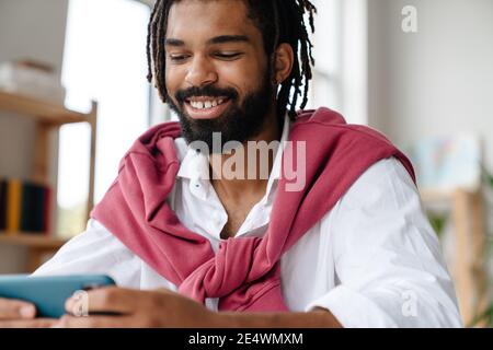 Fröhlich afroamerikanischen Kerl lächeln und spielen Videospiel auf Handy im Büro Stockfoto