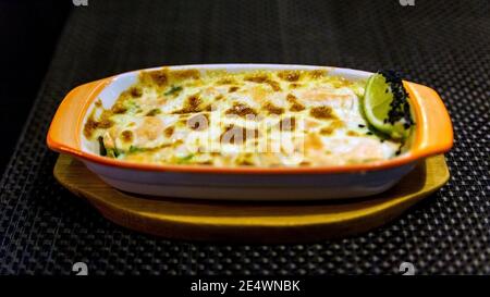 Julienne mit Waldpilzen. Pilze werden in Sahne und mit Käse gebacken. Herbstlaub. Stockfoto