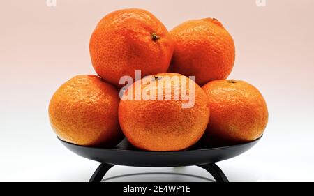 Reife Mandarinen in einer schwarzen Schale isoliert auf weißem Hintergrund. Stockfoto