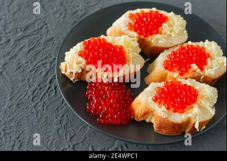 Sandwiches mit rotem Kaviar, Zitrone und Petersilie auf schwarzem Teller auf Betongrund. Meeresfrüchte Stockfoto